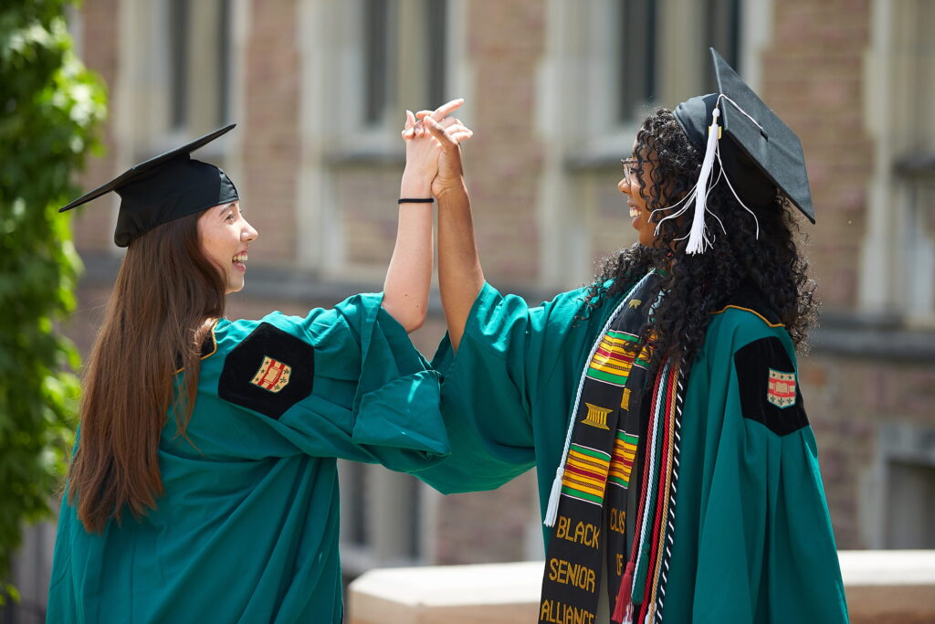 Two students in regalia have a celebratory handshake